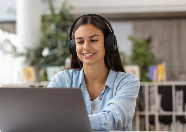 Joven mujer con audífonos revisa su portátil.